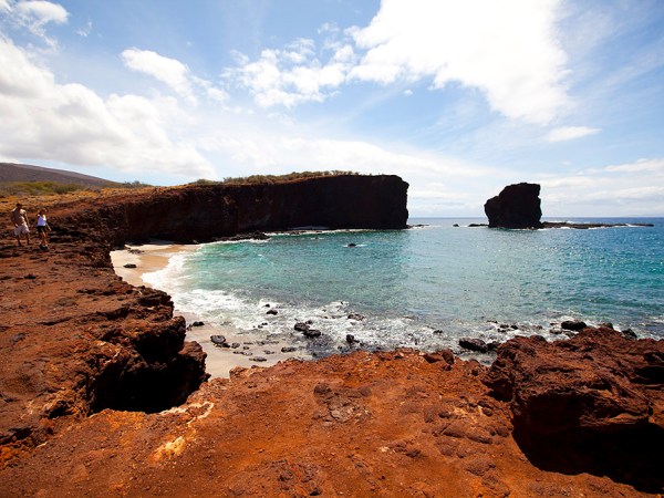 a rocky beach next to a body of water with Lānaʻi in the background